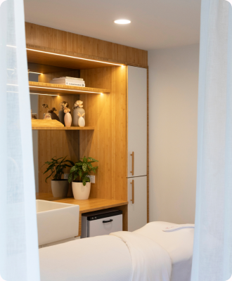 The Cocoon treatment room with a massage bed, warm timber shelving and plants.