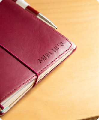 A burgundy leather journal embossed with 'Amélie's' and a pen on a wooden desk.