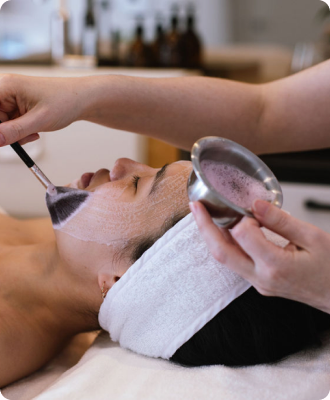 A facialist applying a mask with a brush to a client's face during a facial.