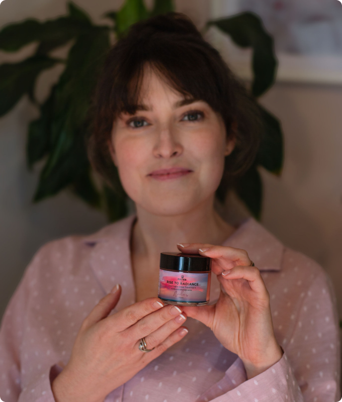 Amélie holding a jar of skincare in front of a leafy green plant.