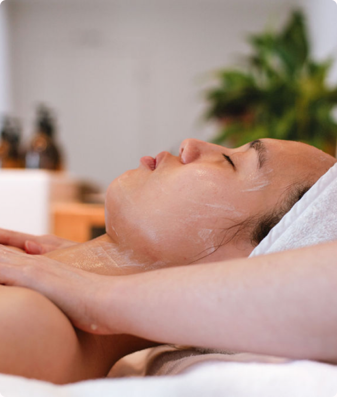 A client resting on a treatment bed during a facial, a plant softly blurred behind.