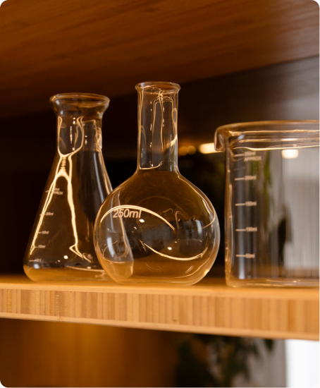 Glass laboratory flasks on a timber shelf, lit warmly.