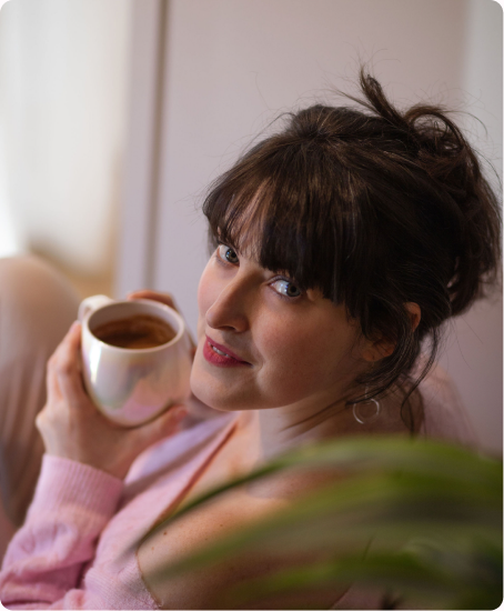 Amélie smiling over a cup of tea in soft pink light.