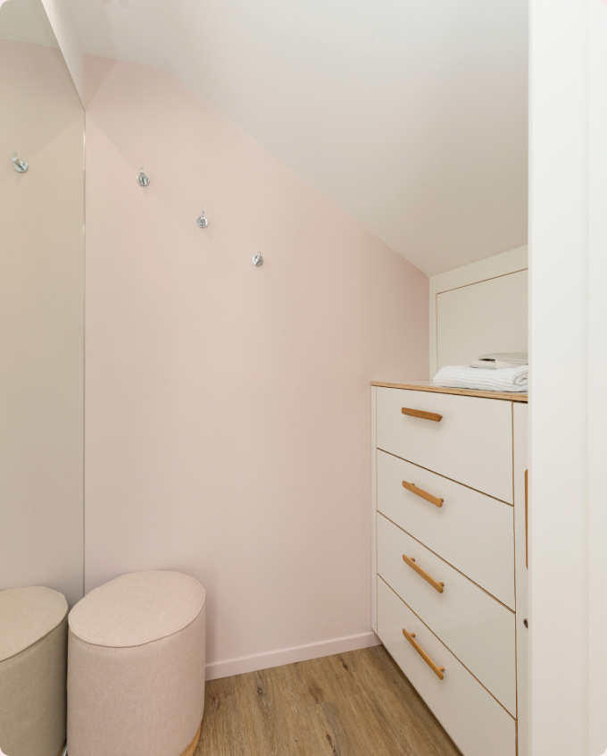 A calm changing room with a chest of drawers and a soft round pouffe.