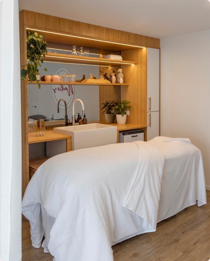 The treatment bed made up in white linen beside a timber wellness station.