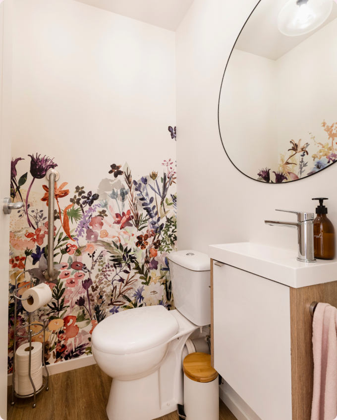 A bright wash room with a floral feature wall, a round mirror and a slim vanity.