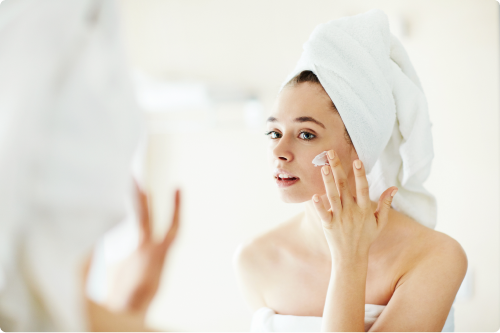 Woman applying cream on her face, wrapped in a bath towel