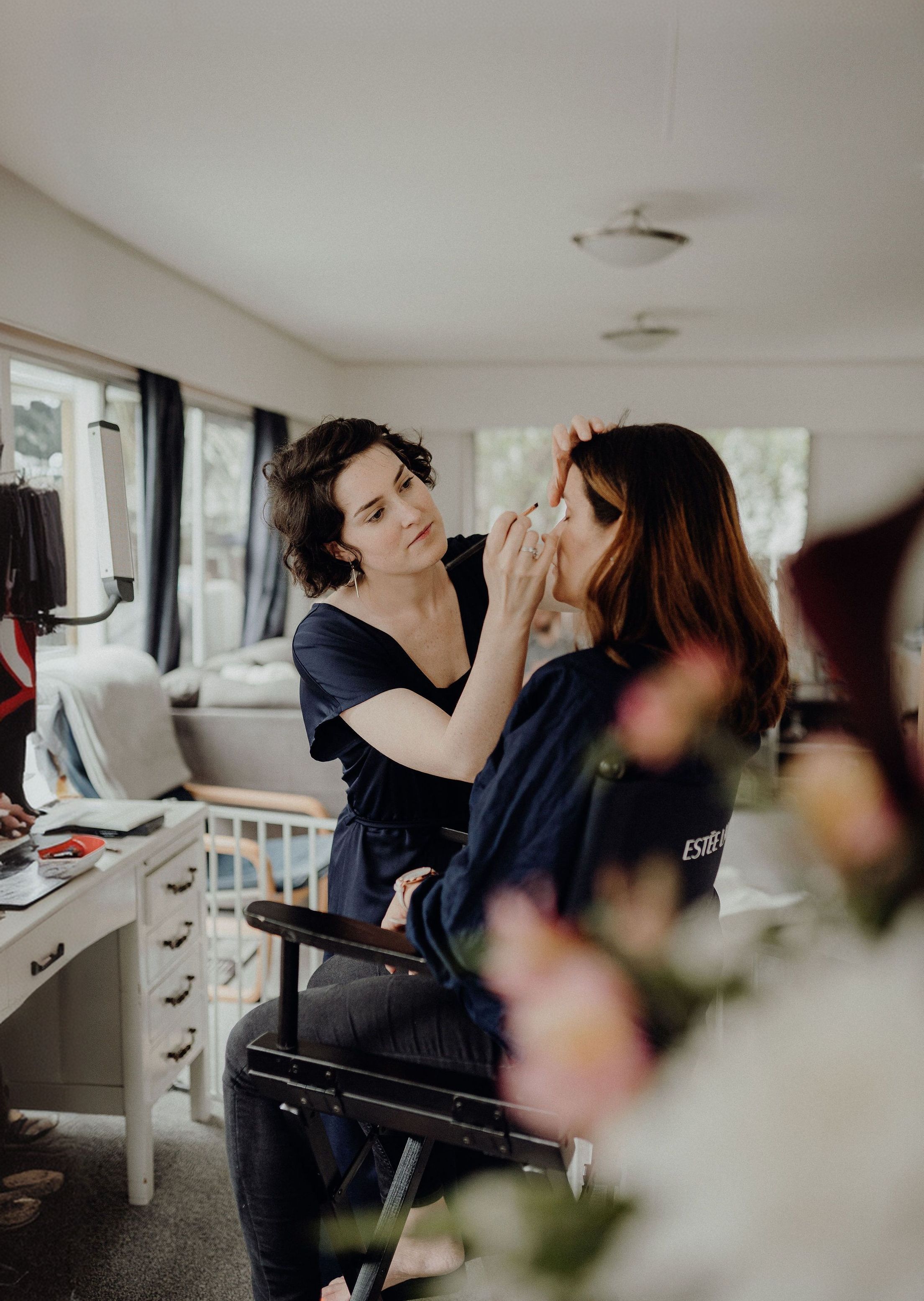 A client learning to apply her own makeup with a hand mirror while Amélie guides her.